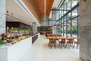 Un comedor amplio con una barra larga que exhibe diversos alimentos, rodeado de mesas y sillas de madera.