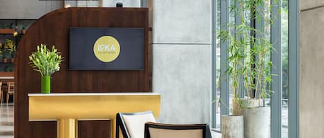 A reception area with a wooden desk, a flat-screen TV, a potted plant, and a large window with a view of bamboo.