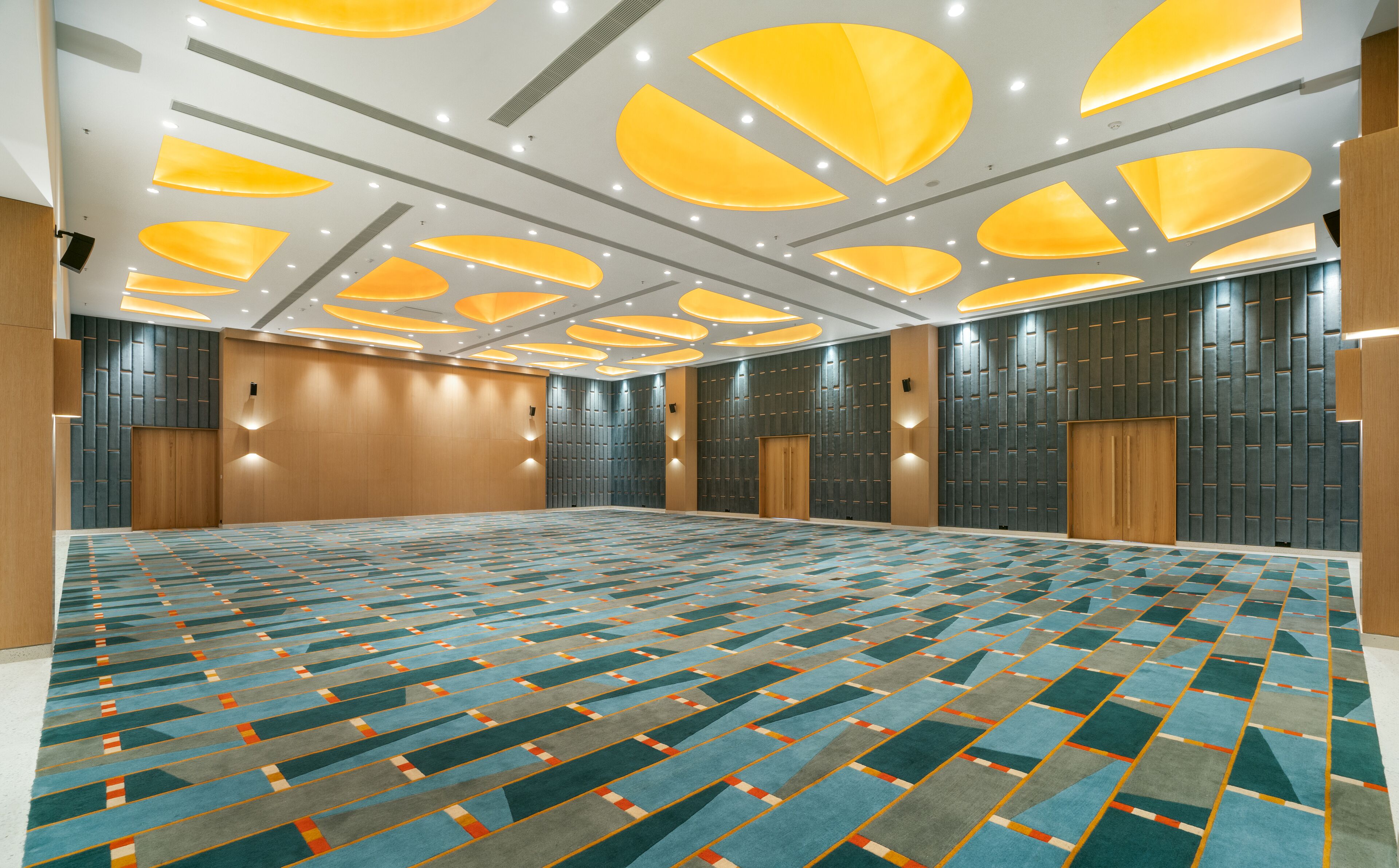 A large, well-lit conference room with a patterned carpet, recessed ceiling lights, and wooden panel walls.