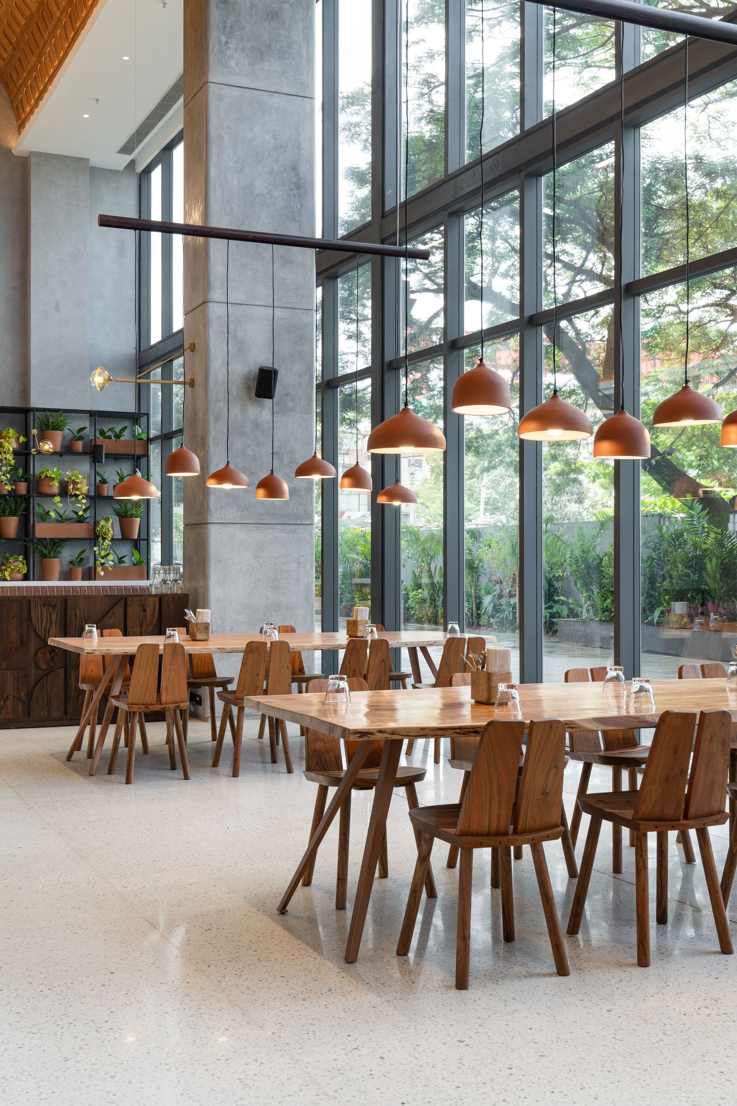 Un comedor amplio con ventanas grandes, mesas y sillas de madera, e iluminación colgante.