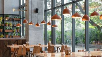 Un comedor amplio con ventanas grandes, mesas y sillas de madera, e iluminación colgante.