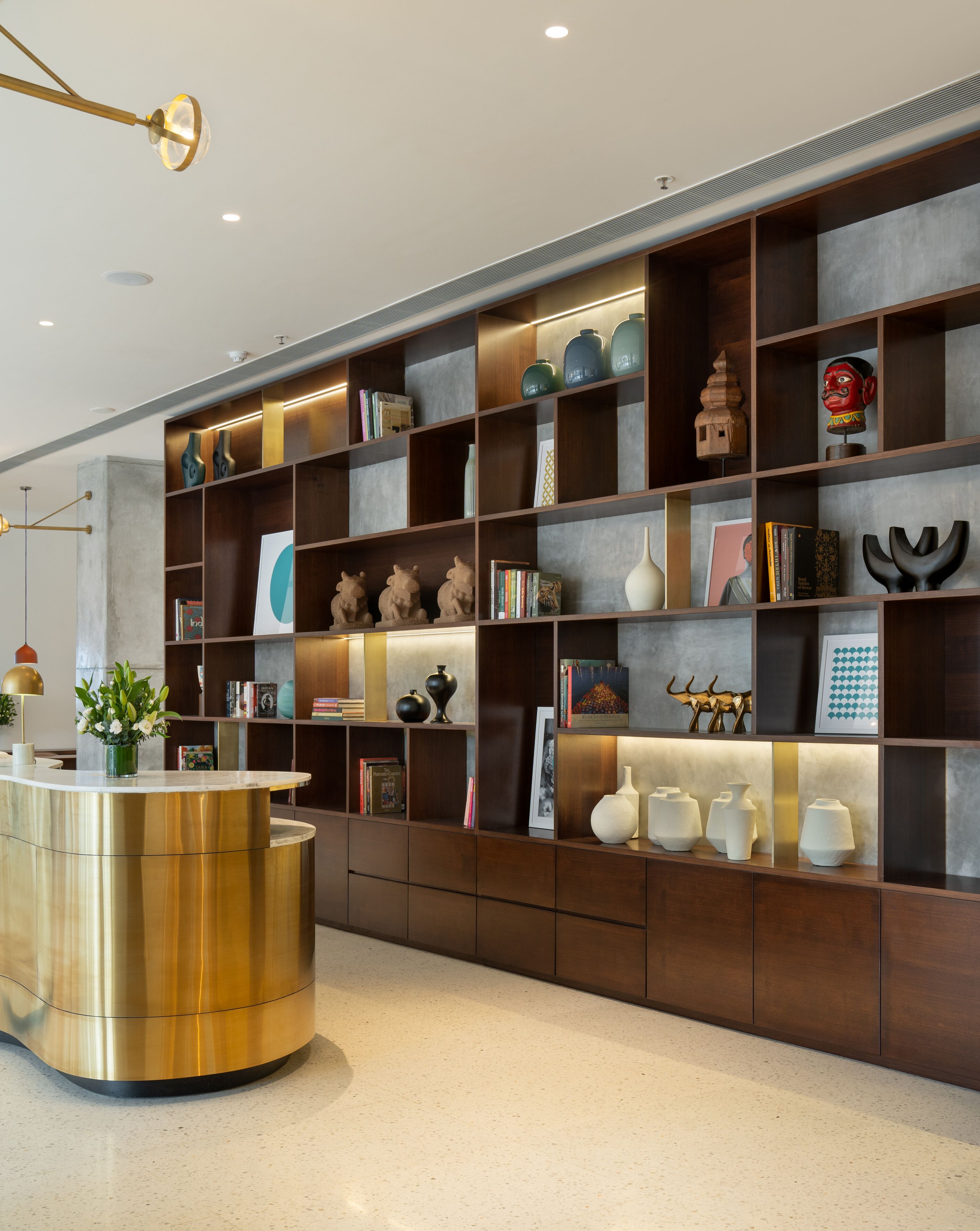 A modern reception area with a gold reception desk, dark wooden shelving with various decorative items, and recessed lighting.