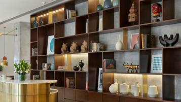 Un área de recepción moderna con un mostrador dorado, estanterías de madera oscura con varios objetos decorativos e iluminación empotrada.