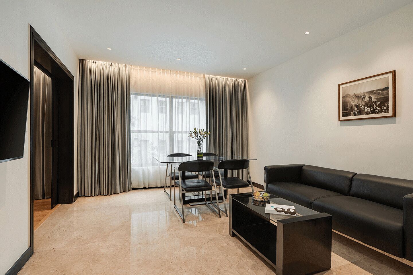 Una sala de estar moderna con un sofá de cuero negro, una mesa de centro de vidrio y una zona de comedor con una mesa y sillas de vidrio.