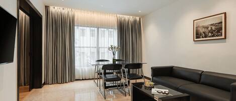 Una sala de estar moderna con un sofá de cuero negro, una mesa de centro de vidrio y una zona de comedor con una mesa y sillas de vidrio.