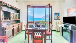 A dining area with a table set for two, a television, and a view of the sea. - La Finestra Sul Lago: Lake Maggiore View & Garden (Stresa)