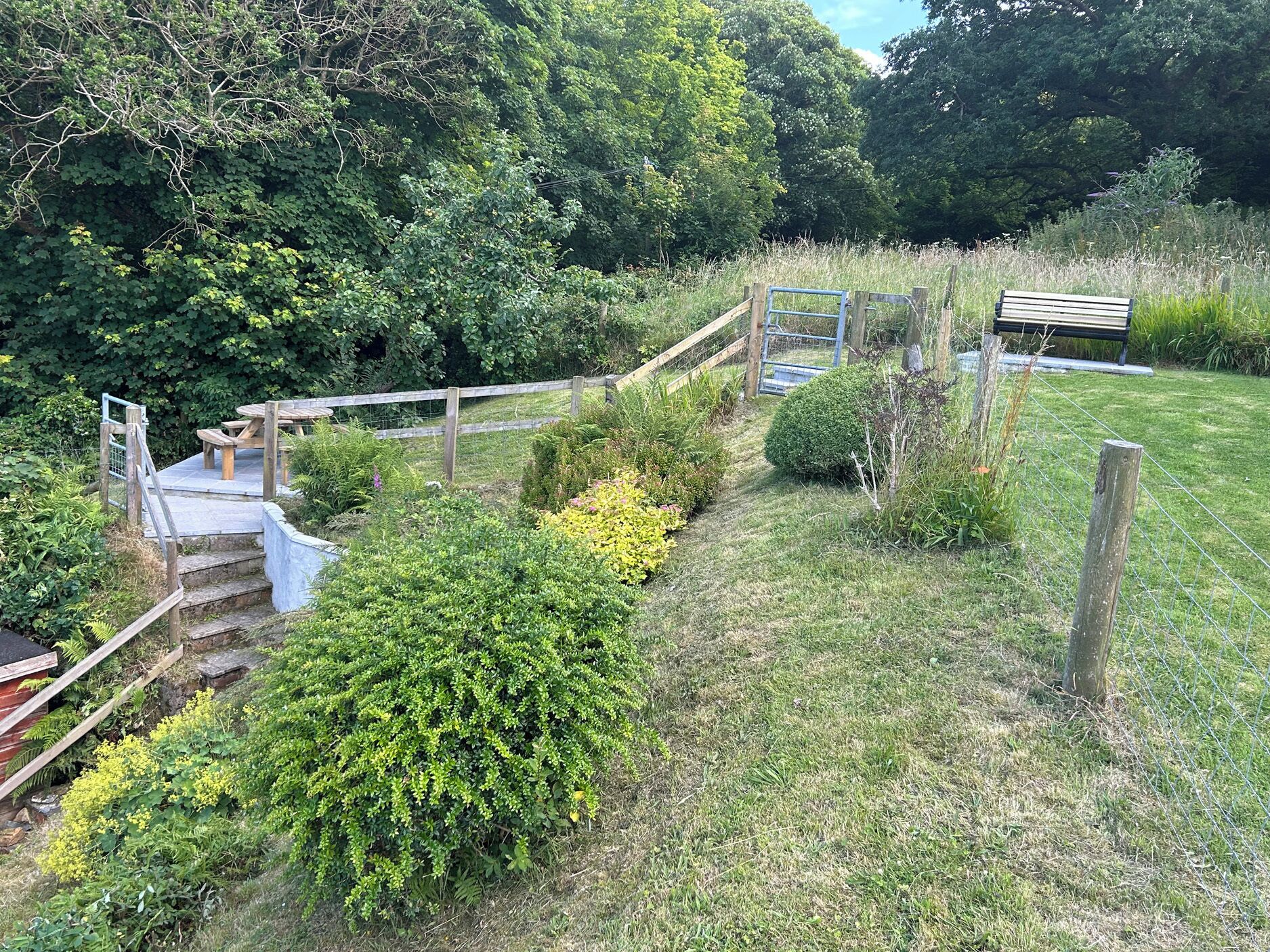 A garden with a wooden bench, a picnic table, and a small wooden staircase leading to a raised area.