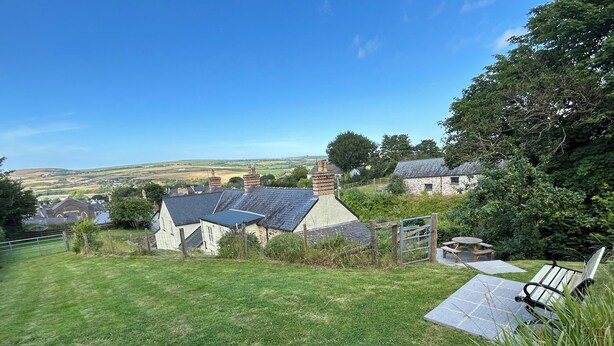 A rural landscape with stone houses, a grassy lawn, and a bench.