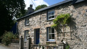A stone building with a blue door and windows, a gated entrance, and a small garden area.