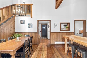 A spacious dining area with wooden flooring, a wooden staircase, and a view into the kitchen.