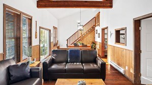 Ein geräumiges Wohnzimmer mit Ledersofa, Holzbalken und einer Treppe, die in einen oberen Bereich führt.