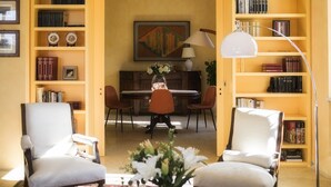 Ein Zimmer mit Esstisch, zwei Stühlen, einer Blumenvase und Bücherregalen voller Bücher.