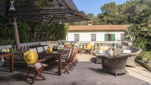 Eine Terrasse im Freien mit Holztischen und -stühlen, einem Korbsessel und einer Pergola.