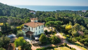Eine große, hell gefärbte Villa mit rotem Ziegeldach, umgeben von üppiger Vegetation und Blick auf die Küste.