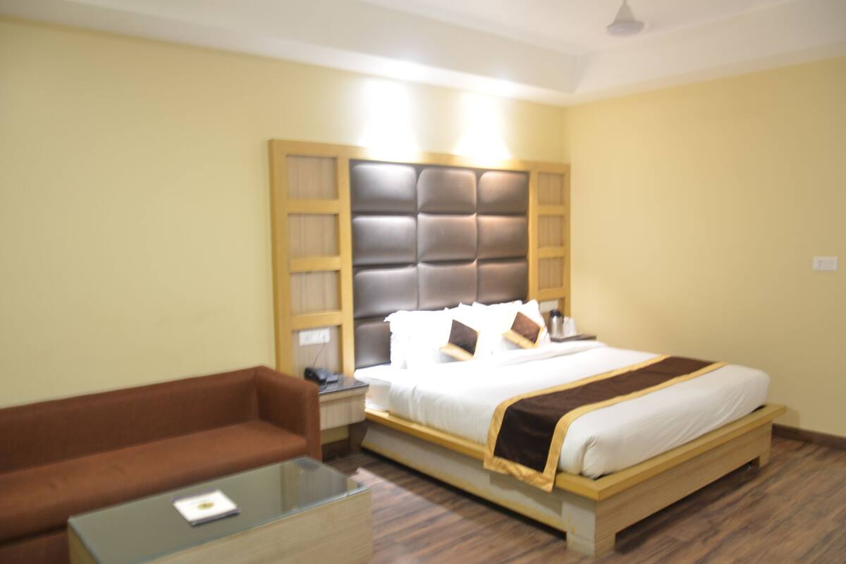 A hotel room with a bed, a brown sofa, a glass coffee table, and a wooden headboard.