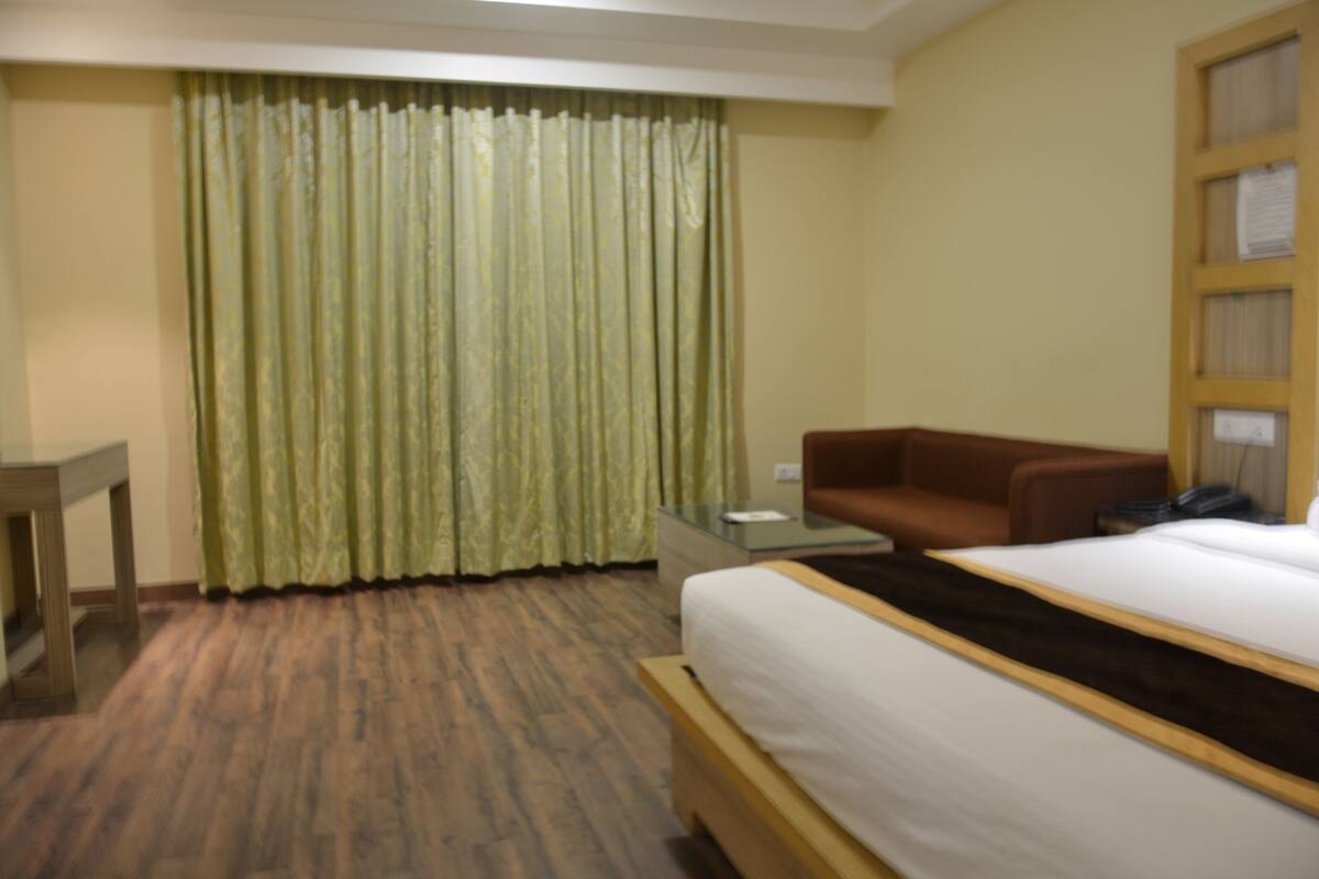 A hotel room with a bed, a brown sofa, a glass table, and a curtain.