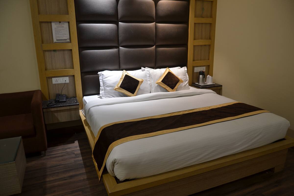 A hotel room with a large bed, wooden headboard, bedside tables, and a desk with a chair.
