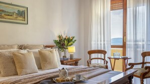A hotel room with a bed, a small table with a lamp, chairs, and a view of the sea. - Sardiniare - Catalogna 62 (Alghero)