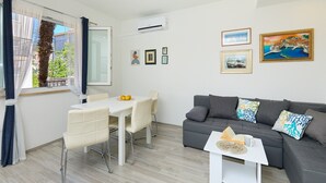 A modern living room with a grey sofa, a dining table with chairs, and a window with curtains. - Apartment Denda (Dubrovnik)