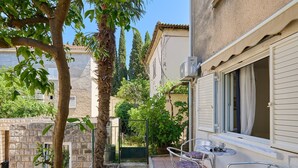 A courtyard with a stone wall, a tree, and a metal table with chairs. - Apartment Denda (Dubrovnik)