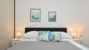 A neatly made bed with white bedding, two bedside tables with lamps, and two framed pictures on the wall. - Apartment Denda (Dubrovnik)