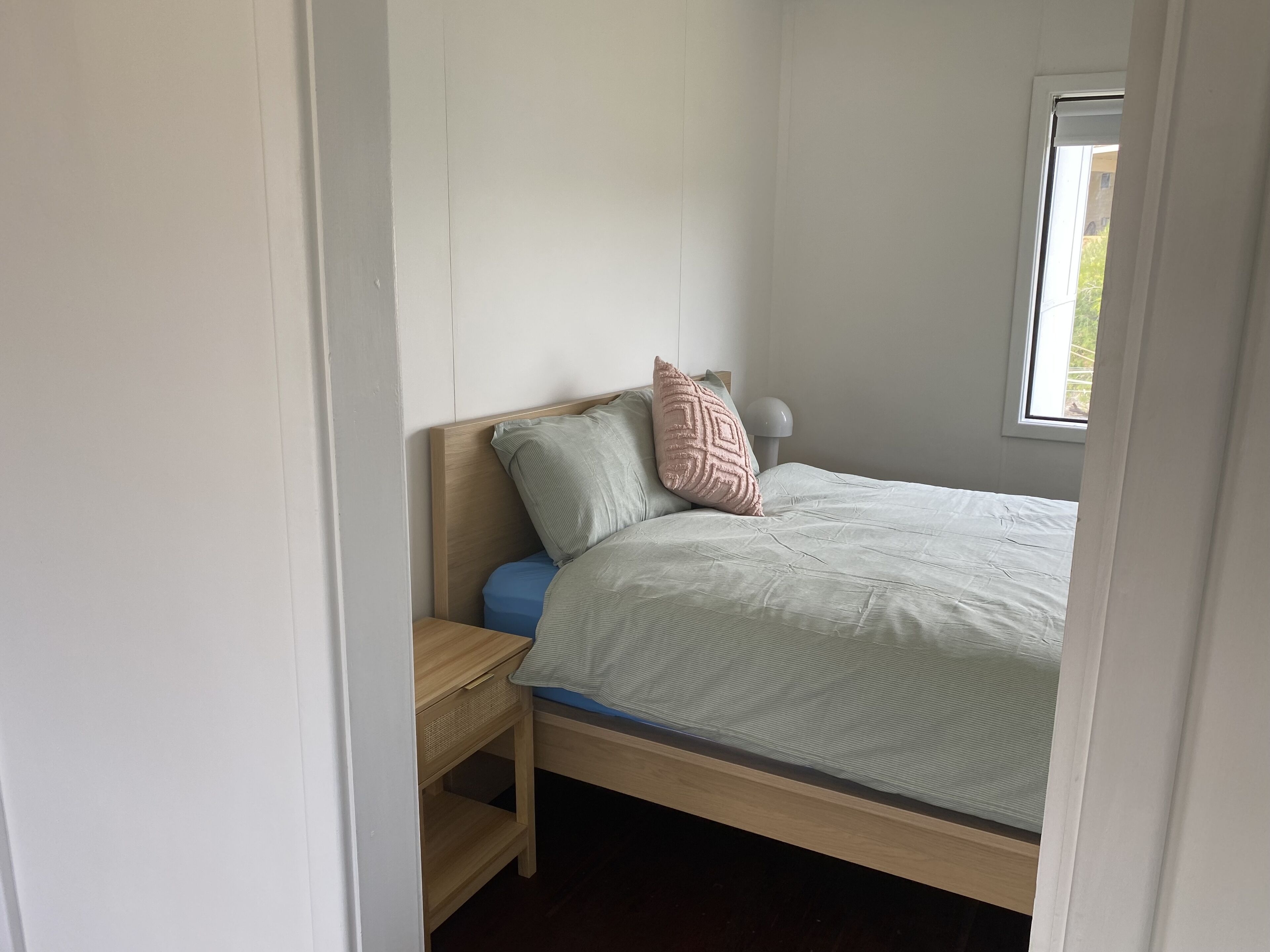 A bedroom with a bed, a nightstand, a window, and a door.