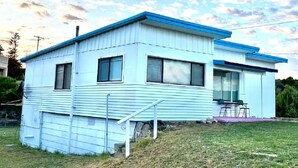Une maison mobile d’un seul étage, de couleur bleu clair, avec un toit bleu, un petit porche doté de deux chaises et une cour gazonnée.