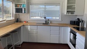 Une cuisine moderne avec des armoires blanches, un plan de travail en bois, une grande fenêtre et un four encastré.