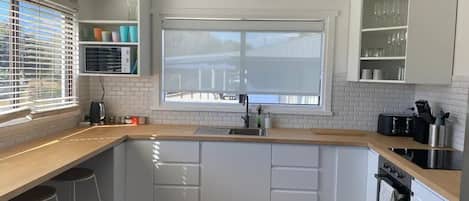 A modern kitchen with white cabinets, a wooden countertop, a large window, and a built-in oven.