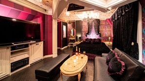 Une chambre luxueuse dotée d’un grand téléviseur à écran plat, d’un coin repas agrémenté d’un lustre, et d’un canapé avec des coussins décoratifs.