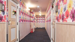 Un couloir d’hôtel avec un papier peint à motifs floraux, des boiseries et un sol recouvert de moquette.