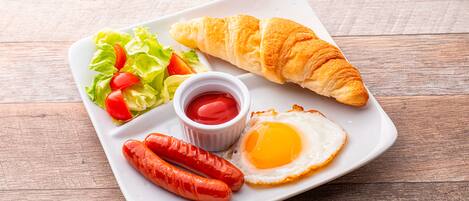 Une assiette comprenant un croissant, deux saucisses, un œuf au plat et une salade composée de tomates et de laitue.