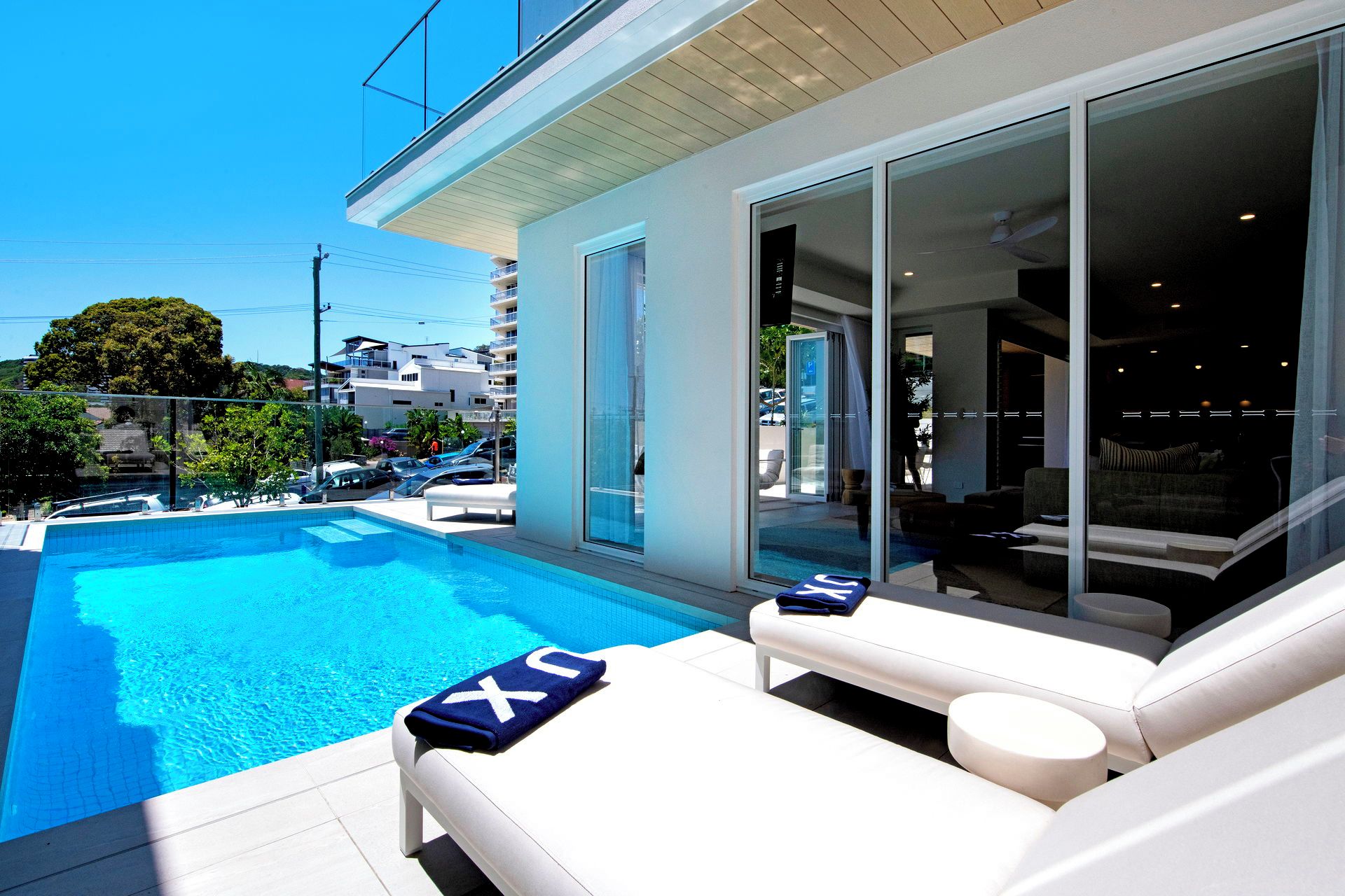 Ein moderner Poolbereich mit freiem Blick auf das Schwimmbecken, ein weißes Outdoor-Sofa und eine Glastür zum Innenbereich.