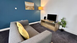 Ein modernes Wohnzimmer mit grauem Sofa, einem HolztV-Schrank, einer Stehlampe und einem Topf mit Pflanze.