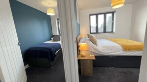 Una habitación pequeña con dos camas, una mesita de noche con lámpara, una ventana con persianas y una puerta con cortina.