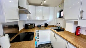 A compact kitchen with white cabinets, a black stove, a sink, and a red fire extinguisher. - 7 Cross Court, Stafford (Stafford)