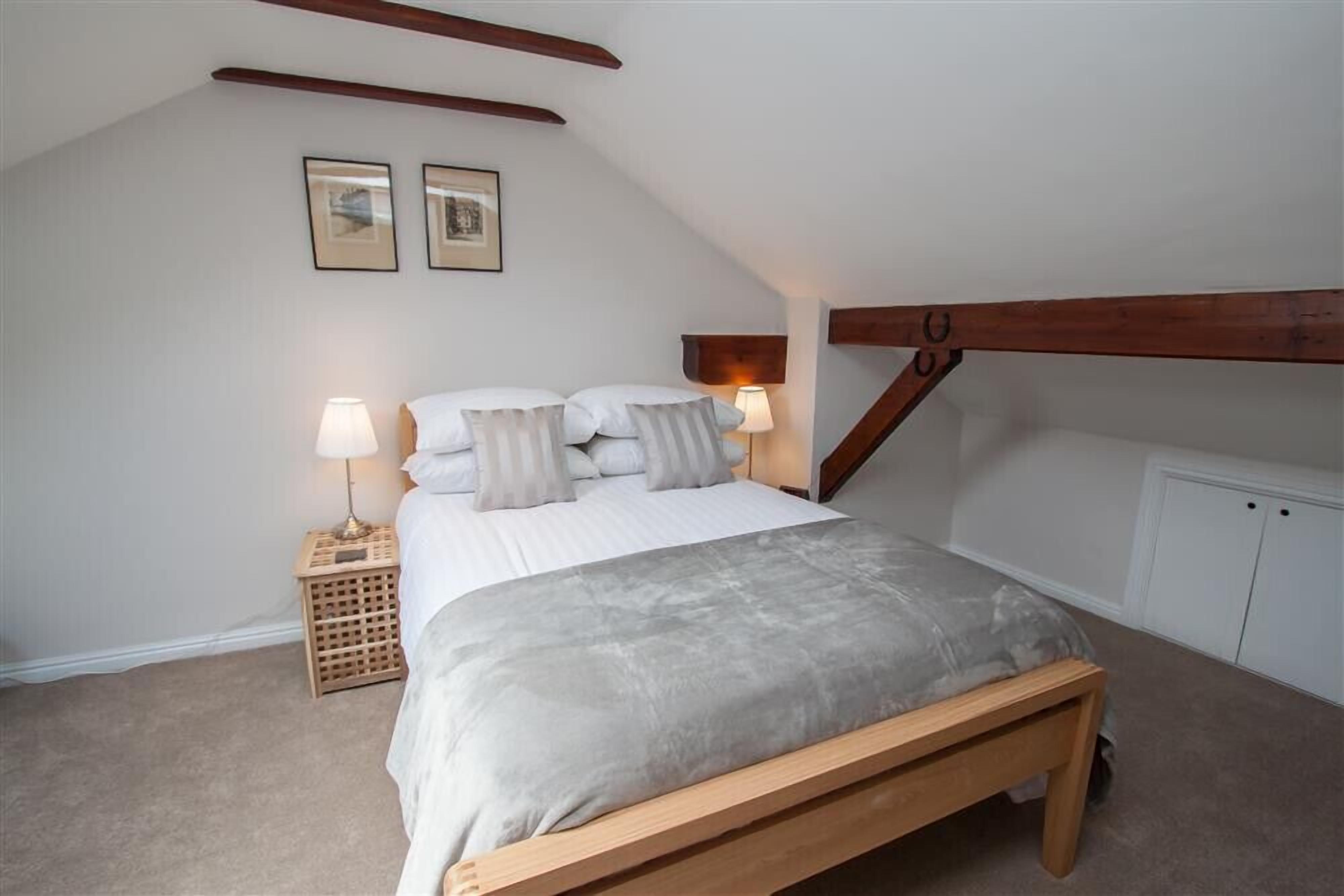 A bedroom with a bed, two bedside lamps, a wooden bench, a small wooden stool, and a white wardrobe.