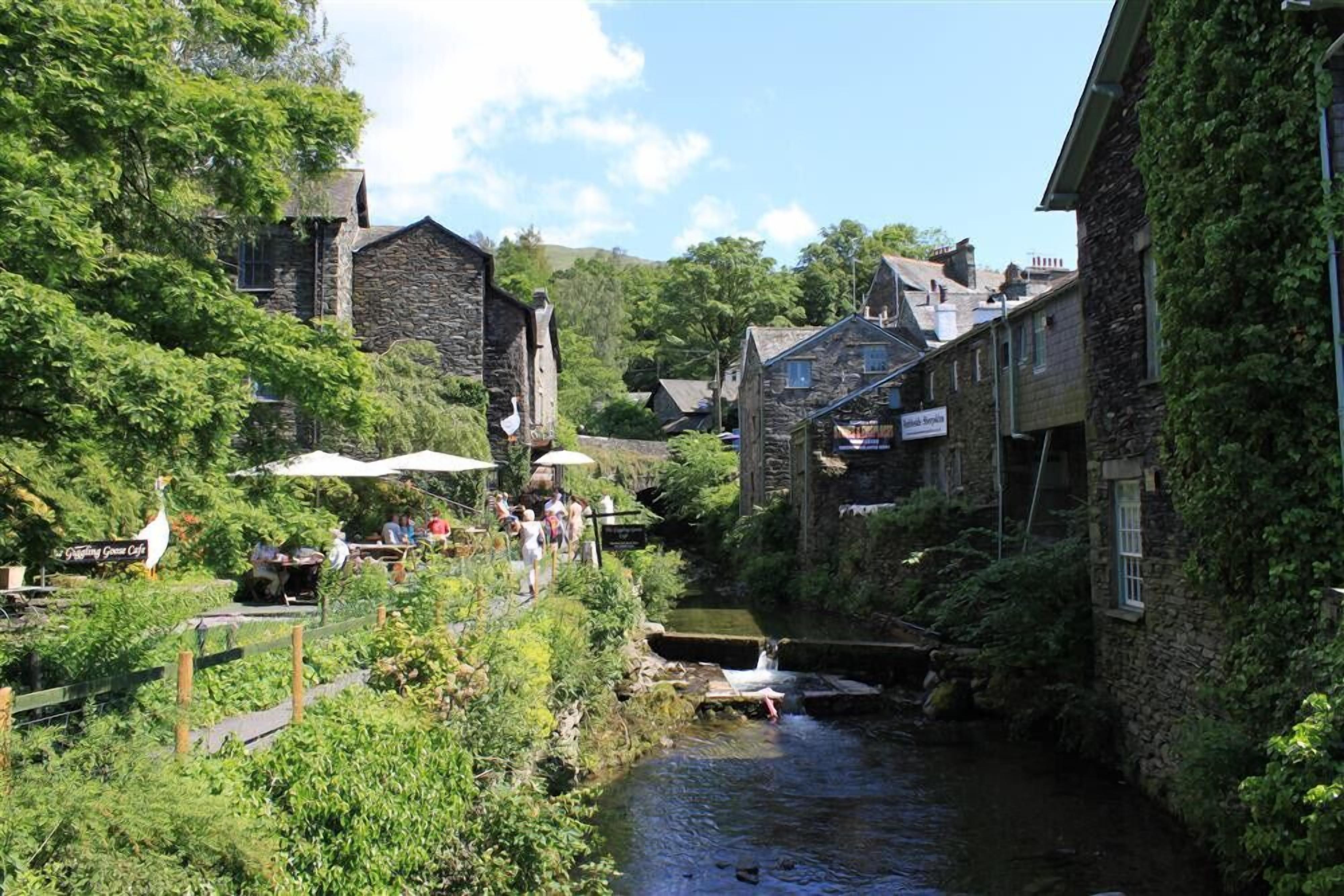 A narrow waterway flanked by stone buildings with outdoor seating areas and a sign for 'The Green Cafe'.