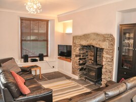 A living room with a stone fireplace, leather sofa, and a television on a shelf.