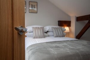 A bedroom with a bed, pillows, a bedside lamp, and a wooden door.