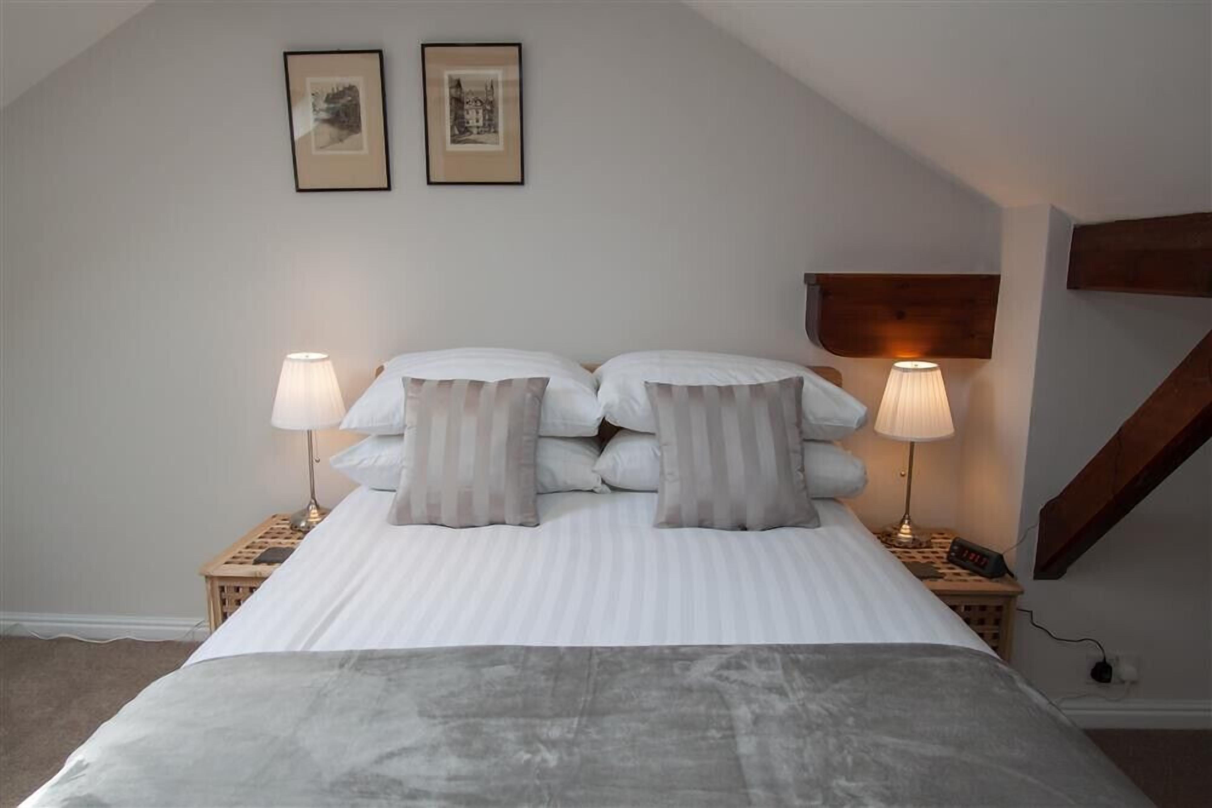 A bedroom with a bed, two bedside lamps, a clock, and two framed pictures on the wall.