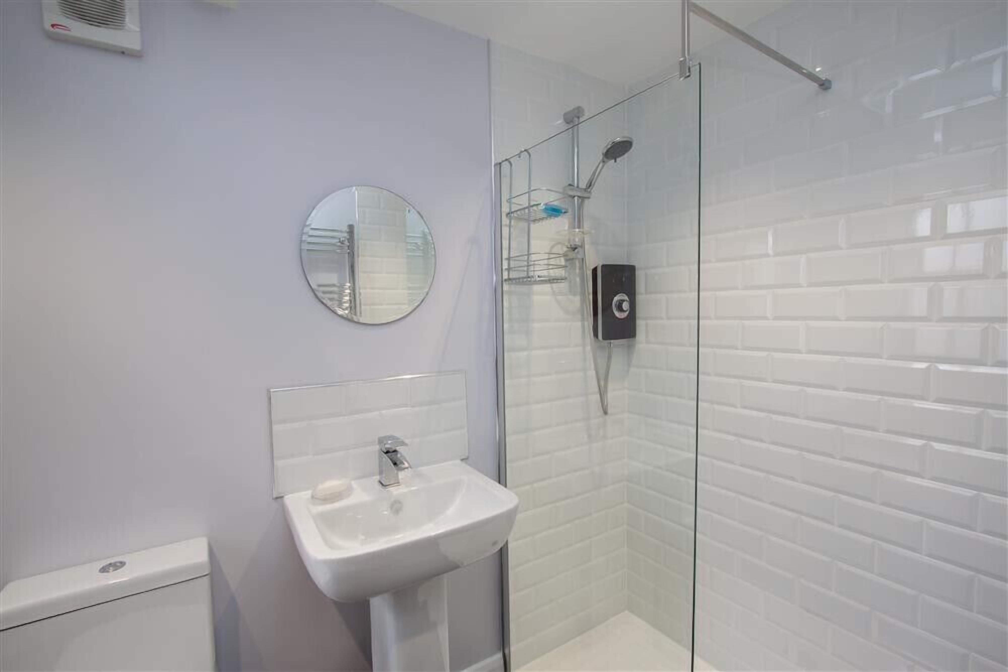 A bathroom with a white sink, a round mirror, and a glass-enclosed shower.