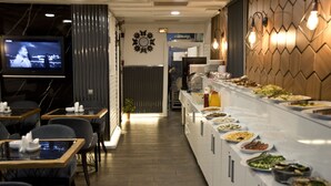 A restaurant with a buffet line, tables, chairs, a TV screen, and a clock on the wall. - Nova City Hotel (Istanbul)