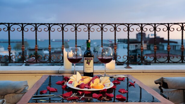 A table with a bottle of wine, two glasses, and a plate of fruit on a balcony overlooking a cityscape. - Nova City Hotel (Istanbul)