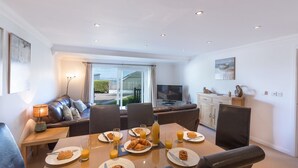 A dining area with a table set for breakfast, including croissants and orange juice, and a sofa with cushions in the background. - Gennaker (St Ives)