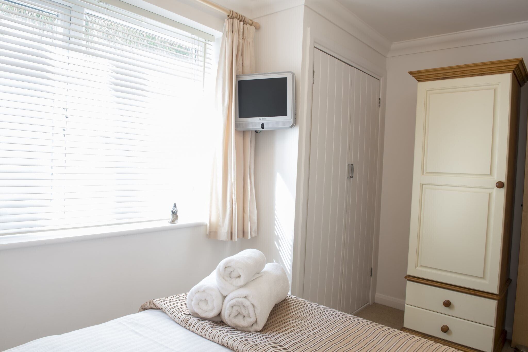 A bedroom with a bed, a TV mounted on the wall, a wardrobe, and a window with curtains.