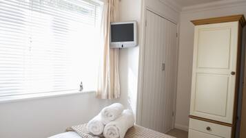 A bedroom with a bed, a TV mounted on the wall, a wardrobe, and a window with curtains.