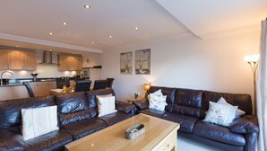 A modern living room with a leather sofa, a glass coffee table, and a kitchen in the background. - Gennaker (St Ives)