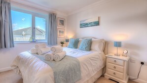 A neatly made bed with rolled towels, a bedside table with a lamp, and a view of the outside. - Gennaker (St Ives)