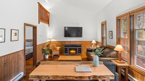 A cozy living room with a fireplace, wooden furniture, and a television mounted on the wall. - Private HOT TUB ~ Nature & Beach at Your Doorstep ⎮ Tidal Pool (Ucluelet)